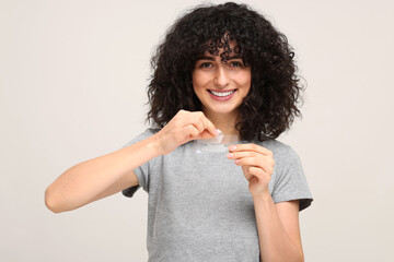 Young woman holding teeth whitening strips on light grey background