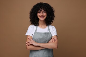 Happy woman wearing kitchen apron on brown background. Mockup for design