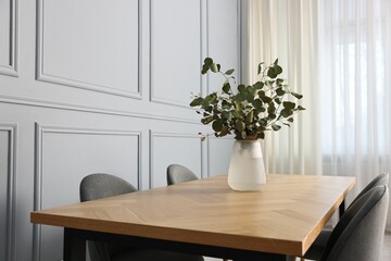 Vase with eucalyptus branches on wooden table in stylish dining room