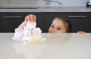 child hides under the table to secretly eat candy. The girl looks at the delicious cookies on...
