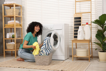 Happy woman putting laundry into washing machine indoors