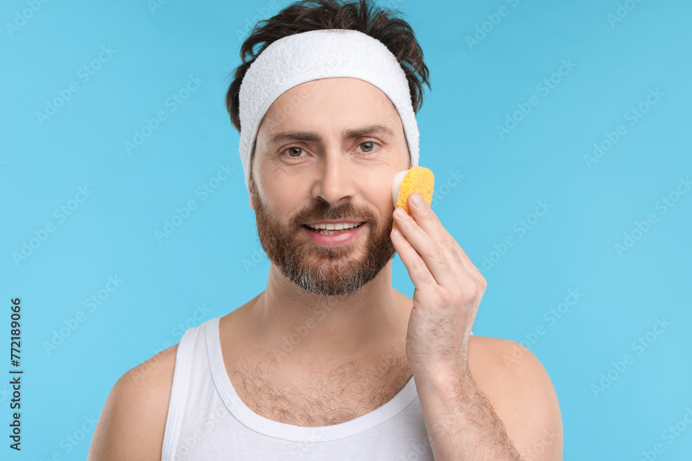 Canvas Prints Man with headband washing his face using sponge on light blue background