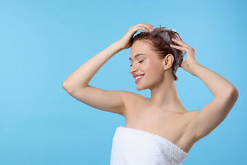 Happy young woman washing her hair with shampoo on light blue background