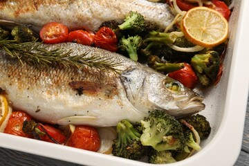 Delicious fish with vegetables and lemon in baking dish on table, closeup