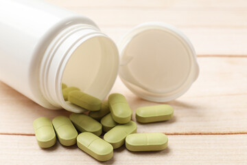 Bottle and vitamin pills on wooden table, closeup