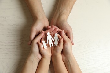 Parents and child holding paper cutout of family at white wooden table, top view