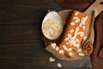 Cake with fresh almond flakes, spoon and nuts on wooden table, top view. Space for text