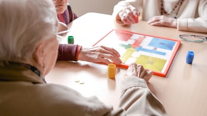 Senior friends playing ludo board game in nursing home