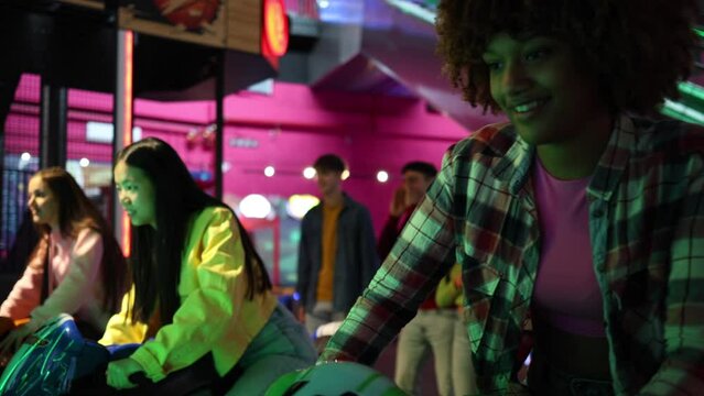 A diverse group of friends is engrossed in playing vibrant motorcycle racing arcade games. Young Adults Enjoying Motorcycle Racing Games at an Arcade