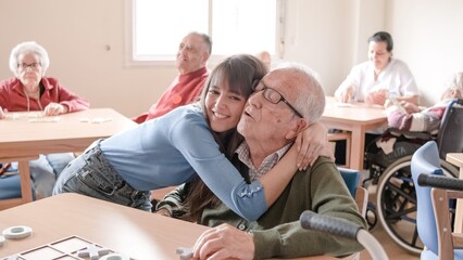 Happy young woman embracing grandfather in nursing home - obrazy, fototapety, plakaty