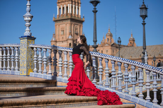 Young, beautiful, brunette woman in black shirt and red skirt, dancing flamenco on the stairs of a beautiful bridge in Spain square in Seville. Flamenco concept, dance, art, typical Spanish.
