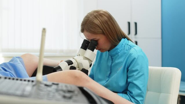 Gynecological office in a modern hospital. The gynecologist uses a colposcope and takes tests from the patient. A woman lies on a gynecological chair during a colposcopy procedure.