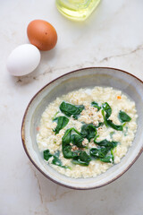 Bowl of stracciatella or italian egg-drop soup with spinach, vertical shot on a light-beige marble background, elevated view