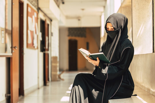 Young teen muslim niqab woman reading the Quran and faith The Holy Al Quran in University building. Arab black chador lady.