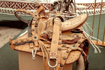 Saddle and handmade leather harness inlaid with metal and stones are sold at a street market with a yurt in the background