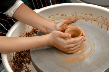 Children's hands create pottery on a potter's wheel during a master class on an outdoor playground