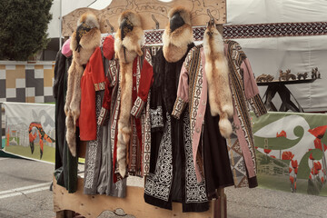 Traditional Kazakh robes and leather hats with natural fur are sold in a street store against the backdrop of a yurt.