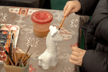Child's hand holds a brush and paints a plaster figure. DIY art project for kids