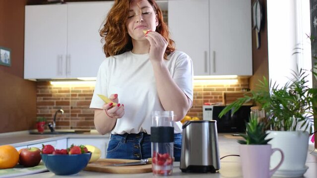 young woman at home in kitchen make fruit smoothie. Beautiful happy young woman in casual home kitchen is preparing fitness cocktail at home. Sporty and vegan meal