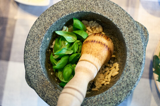 Preparation of traditional Pesto alle Genovese - with basil, olive oil, pine nuts, parmesan cheese and garlic crush in a mortar with a wooden pestle