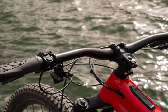 Partial view of an e-bike (handlebar, red frame, tires) by the water - Powered by Adobe