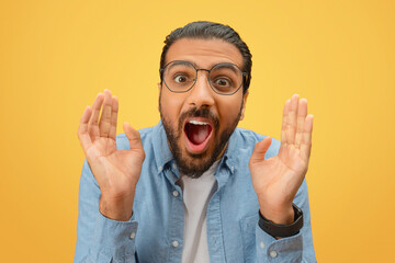 Excited man with hands up on yellow background