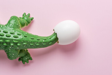 Green crocodile toy with egg shell on pastel pink background. Minimal art concept.
