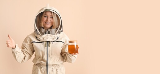 Female beekeeper with jar of sweet honey showing thumb-up gesture on beige background with space...