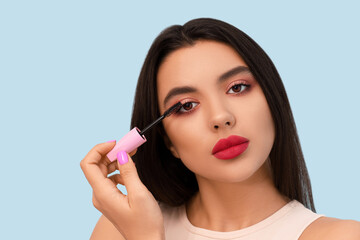 Fototapeta premium Beautiful young woman with stylish mascara on blue background