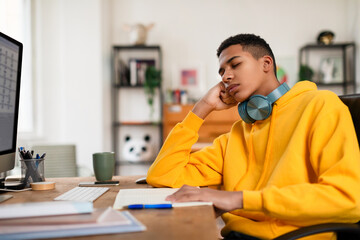 Tired black teen guy resting at desk with computer