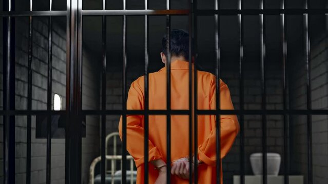 Back View Of Asian Male Prisoner Try To Take The Handcuffs Off While Standing In Prison