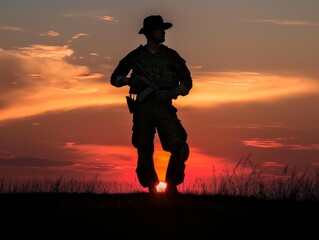 A man in a military uniform stands in the grass at sunset. The sky is orange and the sun is setting