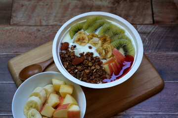 Fresh fruit and granola with yogurt in a bowl on a wooden table.