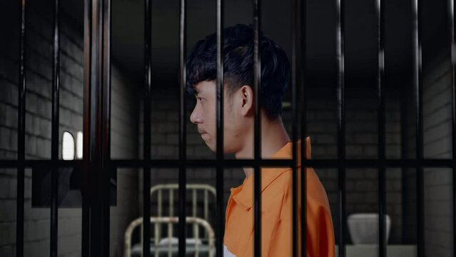 Close Up Side View Of Asian Male Prisoner Standing In Prison, Raising Head And Looking To Camera In Anger