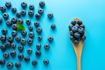 Tasty ripe blueberries on blue background with a spoon. Minimal food concept. Flat lay.