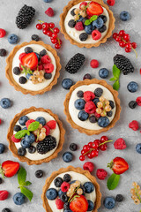 Tartlets with custard vanilla cream with fresh berries and mint on a gray concrete background. Summer dessert.