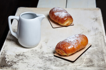 Homemade buns with jam with powdered sugar on wooden background. Fresh bakery and milk jug on kitchen table. Sweet breakfast