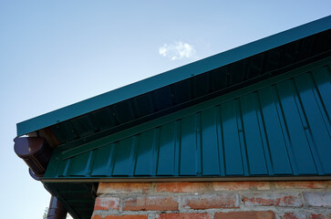 Fragment of metal roofing of rural building. Holder gutter drainage system on the roof