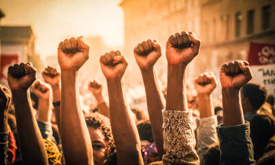 Crowd gathers in city streets, raising clenched fists in unison, symbolizing unity and resistance. Placards are visible, displaying messages advocating for social change - obrazy, fototapety, plakaty
