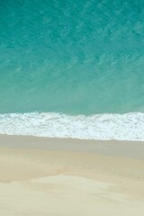 Vertical shot of a sandy beach coastline, with soft, rolling waves of the ocean lapping onto shore