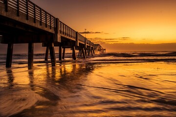 Fototapeta na wymiar Wooden pier jutting out into a pristine beach, with a sunset illuminating the horizon