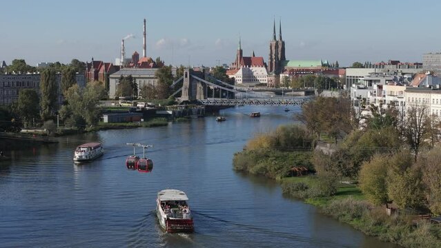 Wroclaw scenic drone aerial view of river Odra with tourists boats and crossing cable cars at summer or spring time and Grunwald Bridge in background with Cathedral at Tumski Island