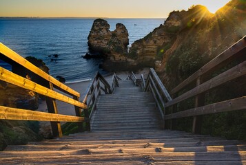 Idyllic scene in Lagos, Portugal of a set of wooden steps leading down to a sandy beach at sunset.