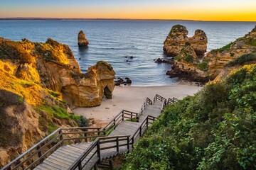 Idyllic scene in Lagos, Portugal of a set of wooden steps leading down to a sandy beach at sunset.