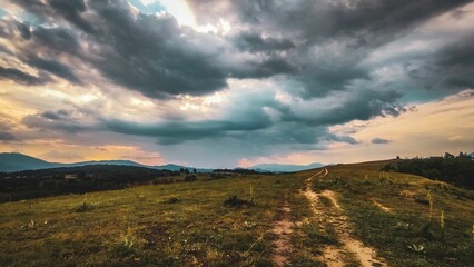 Tranquil dirt road in a golden field, bathed in warm, glowing sunlight and framed by dramatic clouds