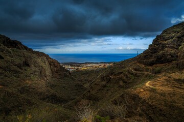 Small residential area on the shore visible through rugged mountains with dramatic clouds above