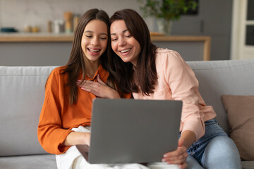 Happy mother and teen daughter looking at laptop, doing online shopping or watching movie using...