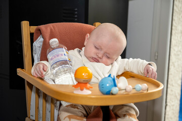 bébé en train de dormir sur sa chaise haute avec une bouteille d'eau dans les bras
