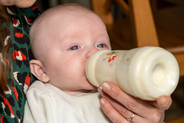 bébé en train de boire son biberon  dans les bras de sa mère