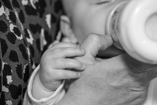 détail d'une mains de bébé et de sa mère pendant que le bébé bois un biberon